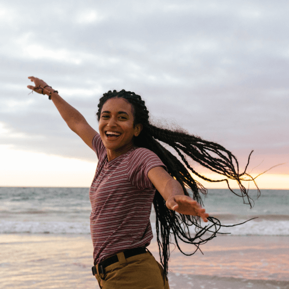 Young woman running down the beach near the ocean during sunset, smiling