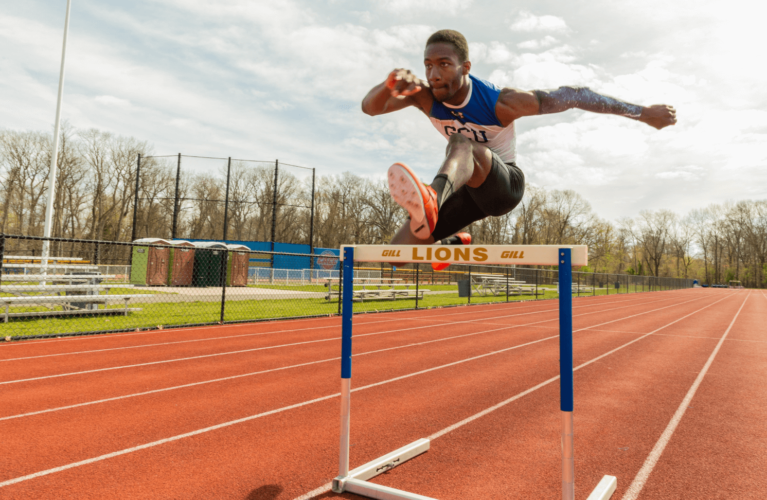 Student athlete jumping hurdle on running track