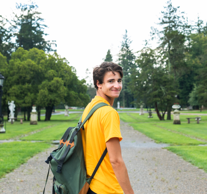 Young man in gardens on a path looking back over his shoulder and smiling