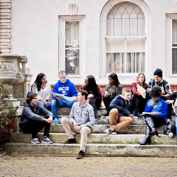 Group of 10 diverse students sitting on steps outside talking and reading notbooks